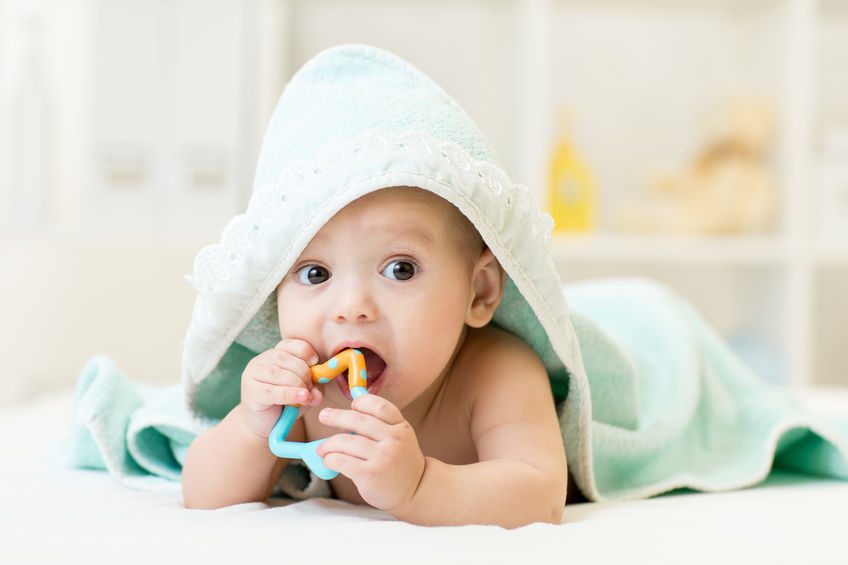 baby with teether in mouth under bathing towel at nursery